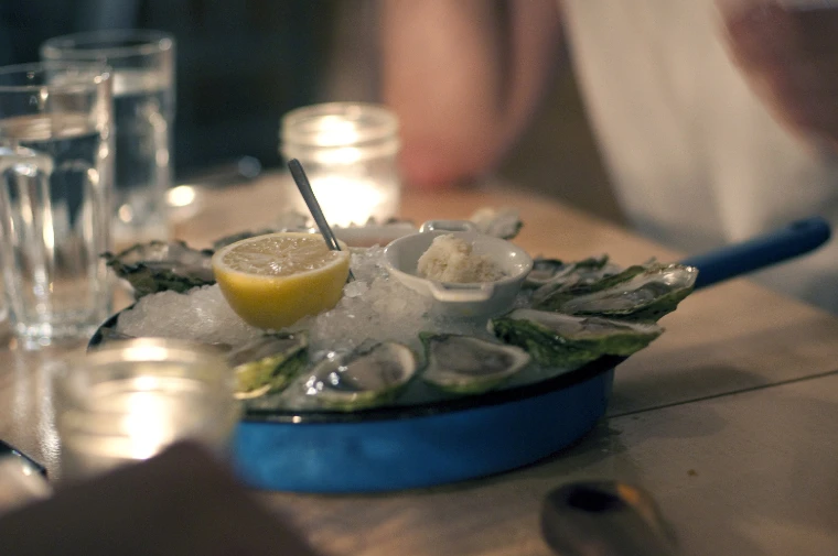 Opened oysters on crushed ice in a blue pan with half a lemon and a small dish of grated horseradish, on a table lit by candles in glass jars (2012).