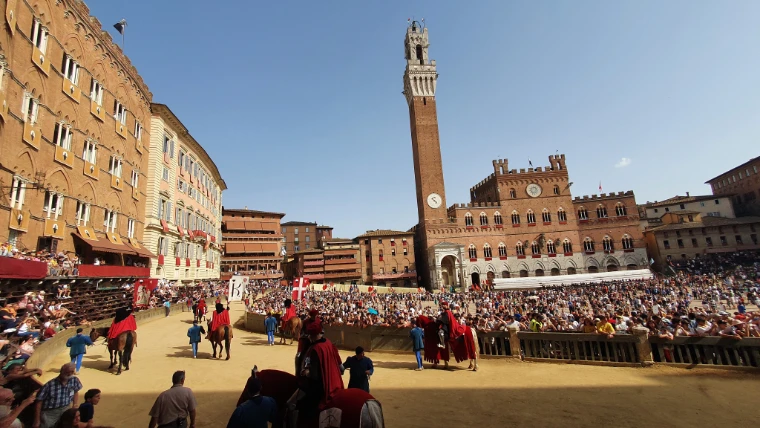The Torre del Mangia and the Palazzo Pubblico above the Campo, the stands full and the pageant on the track (August 2022).