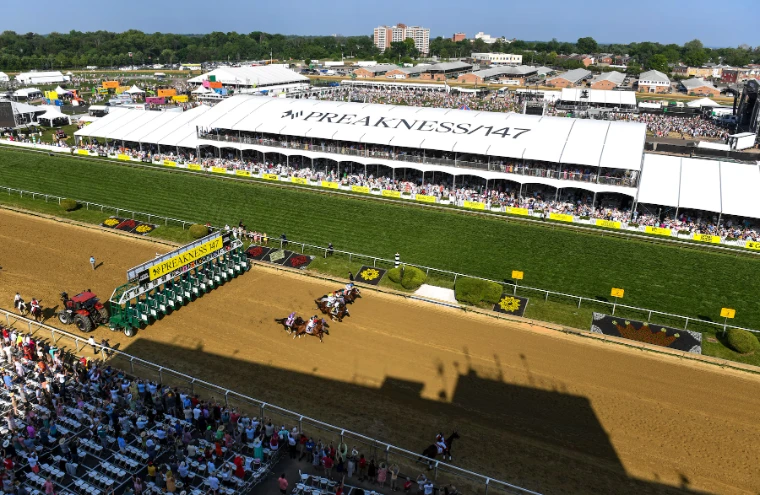 The field breaks from the gate before the white tents and packed stands of the Preakness, seen from above, in 2022. The Preakness Stakes at Pimlico, Baltimore, in the season calendar of The Mansa Court