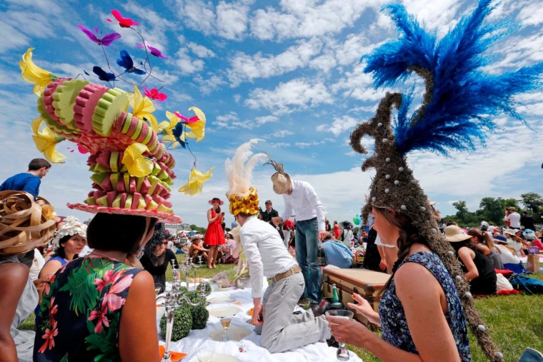Racegoers in extravagant feathered and flowered hats picnicking on the lawn with silver candelabra and champagne at the Prix de Diane, Chantilly, the June race in the season calendar of The Mansa Court