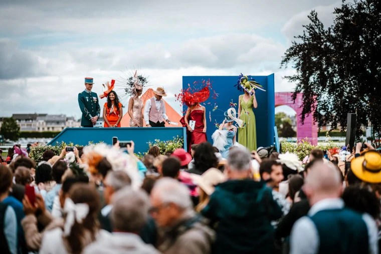Finalists in sculptural hats and gowns on the stage of the hat competition before the crowd at the Prix de Diane in Chantilly, a mid-June engagement in the season calendar of The Mansa Court