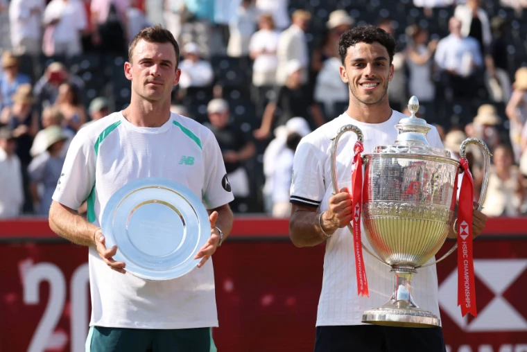 Francisco Cerúndolo holds the trophy beside Tommy Paul with the runner-up’s plate. The Queen’s Club Championships, The Queen’s Club, London, June 2026, in the season calendar of The Mansa Court