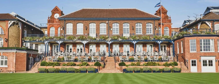 The red-brick Members’ Clubhouse and its terrace, seen across the lawn. The Queen’s Club, West Kensington, London, shown for The Queen’s Club Championships in the season calendar of The Mansa Court
