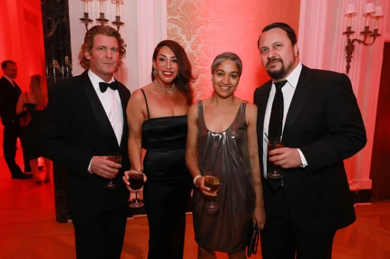 Four guests in black tie and evening dress in a red-lit room of damask walls and brass sconces at The Sailors Ball in New York, an April engagement in the season calendar of The Mansa Court