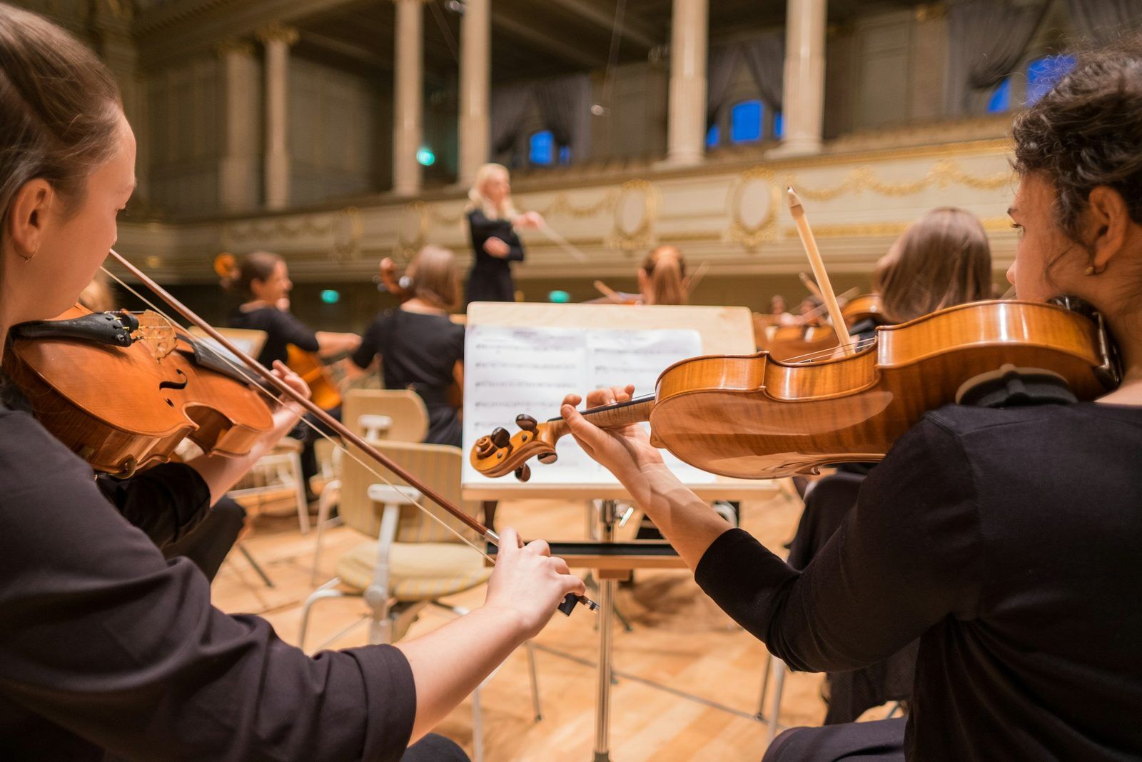 Violinists playing from the desk before the conductor in a gilded hall, the private recital The Mansa Court holds for members at The Salon de Musique in New York