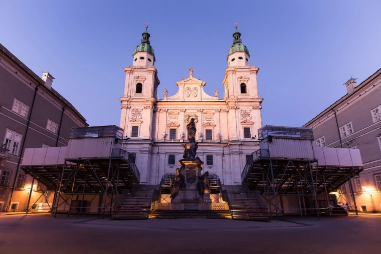 Salzburg Cathedral’s twin-towered facade glows pink at dusk above the lit grandstand built on the Domplatz for Jedermann (2016).