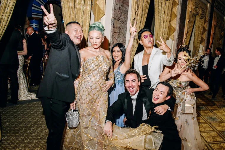Guests in black tie and embellished gowns, one holding a gilded mask, celebrating among gold curtains and marble columns at The Save Venice Ball in New York, a late-April engagement in the season calendar of The Mansa Court