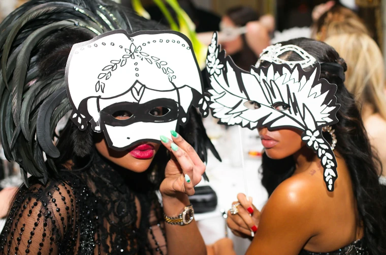 Two guests holding up black-and-white Venetian masks at dinner at The Save Venice Ball in New York, a late-April engagement in the season calendar of The Mansa Court