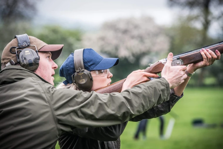 A shooting instructor steadying a member’s over-and-under shotgun as she mounts to a clay at the shooting ground in Millbrook, The Shooting School hosted by The Mansa Court each mid April