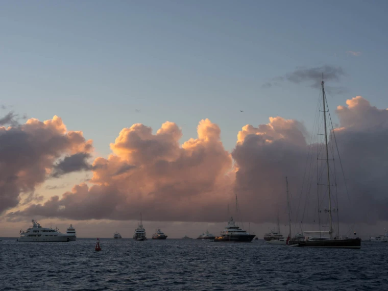 Superyachts and a tall sailing yacht at anchor off the island at sunset, pink clouds over the sea (2013).