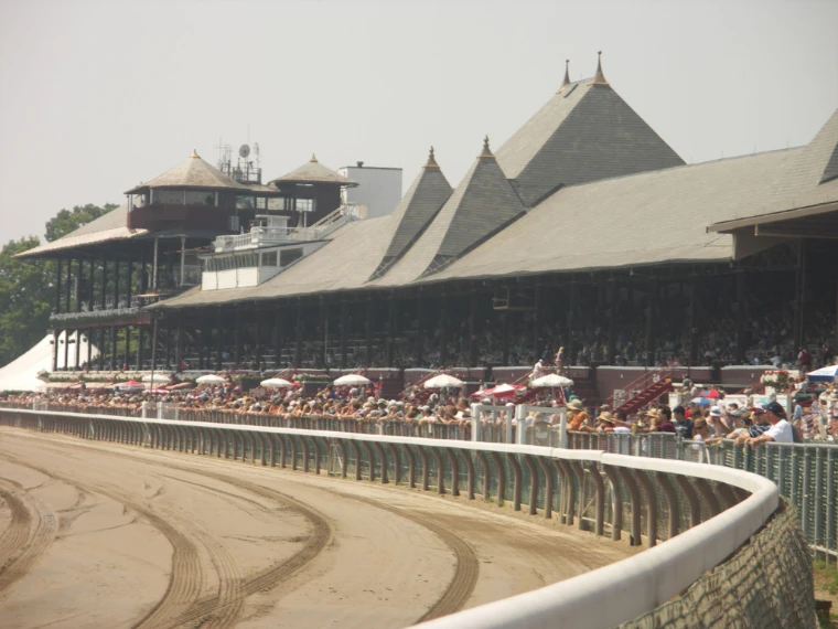 The long Saratoga grandstand with its pointed slate roofs and cupolas, packed with spectators, curves around the dirt track on a hazy summer day (2005).
