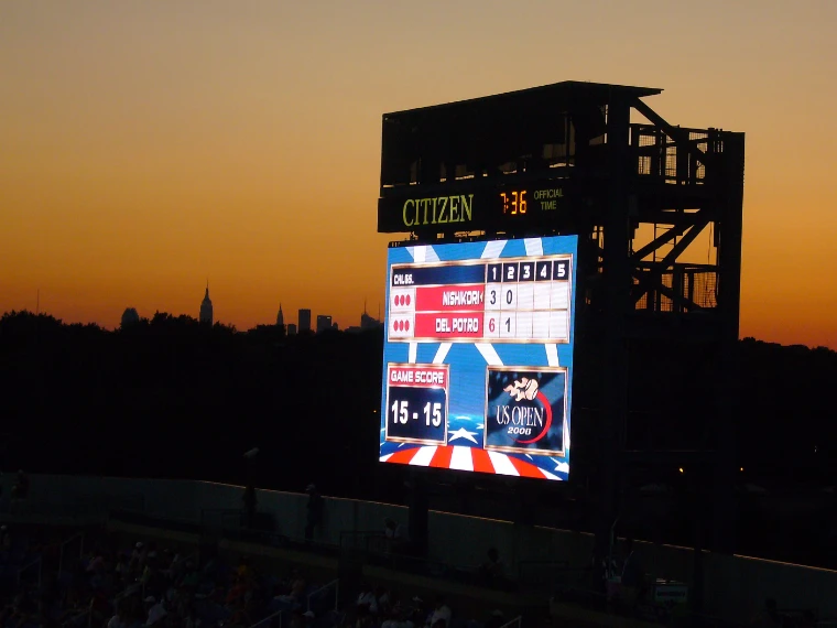 A lit stadium scoreboard stands against an orange dusk sky, with the Manhattan skyline in silhouette on the horizon (2008).