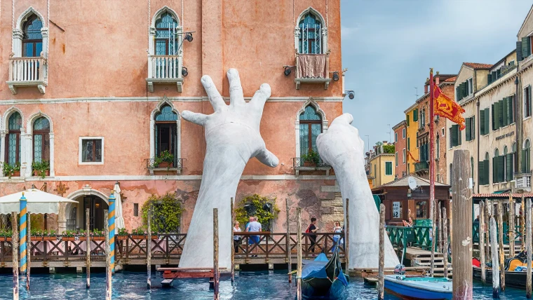 Lorenzo Quinn’s Support, two giant white hands rising from the Grand Canal against the pink façade of Ca’ Sagredo during the Venice Biennale, an engagement in the season calendar of The Mansa Court