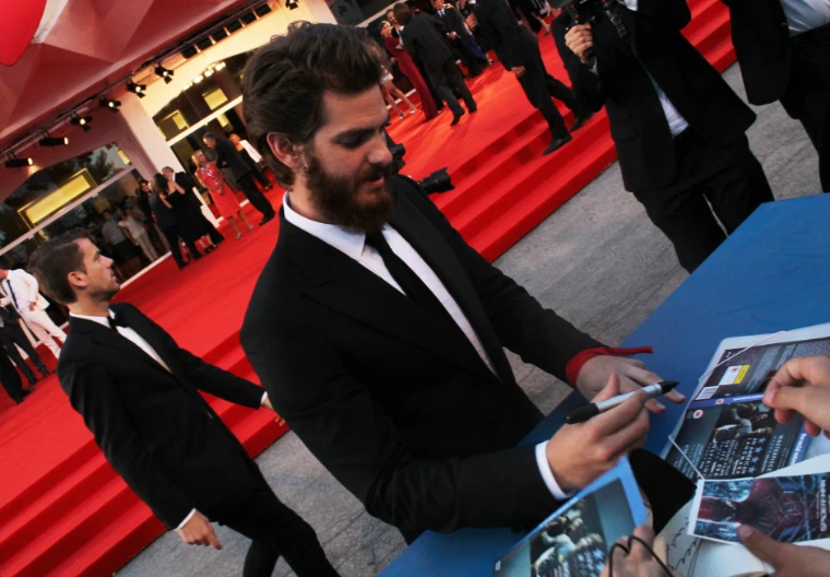 An actor signs autographs for fans along the red carpet, with photographers and guests behind him (2014).