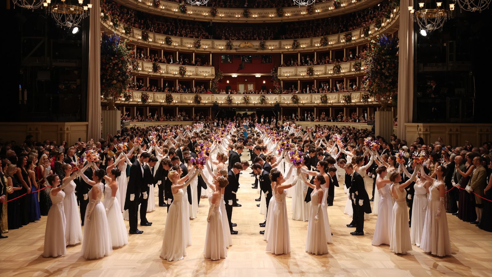 Debutantes raising their bouquets on the ballroom floor below the flower-hung tiers of boxes at The Vienna Opera Ball