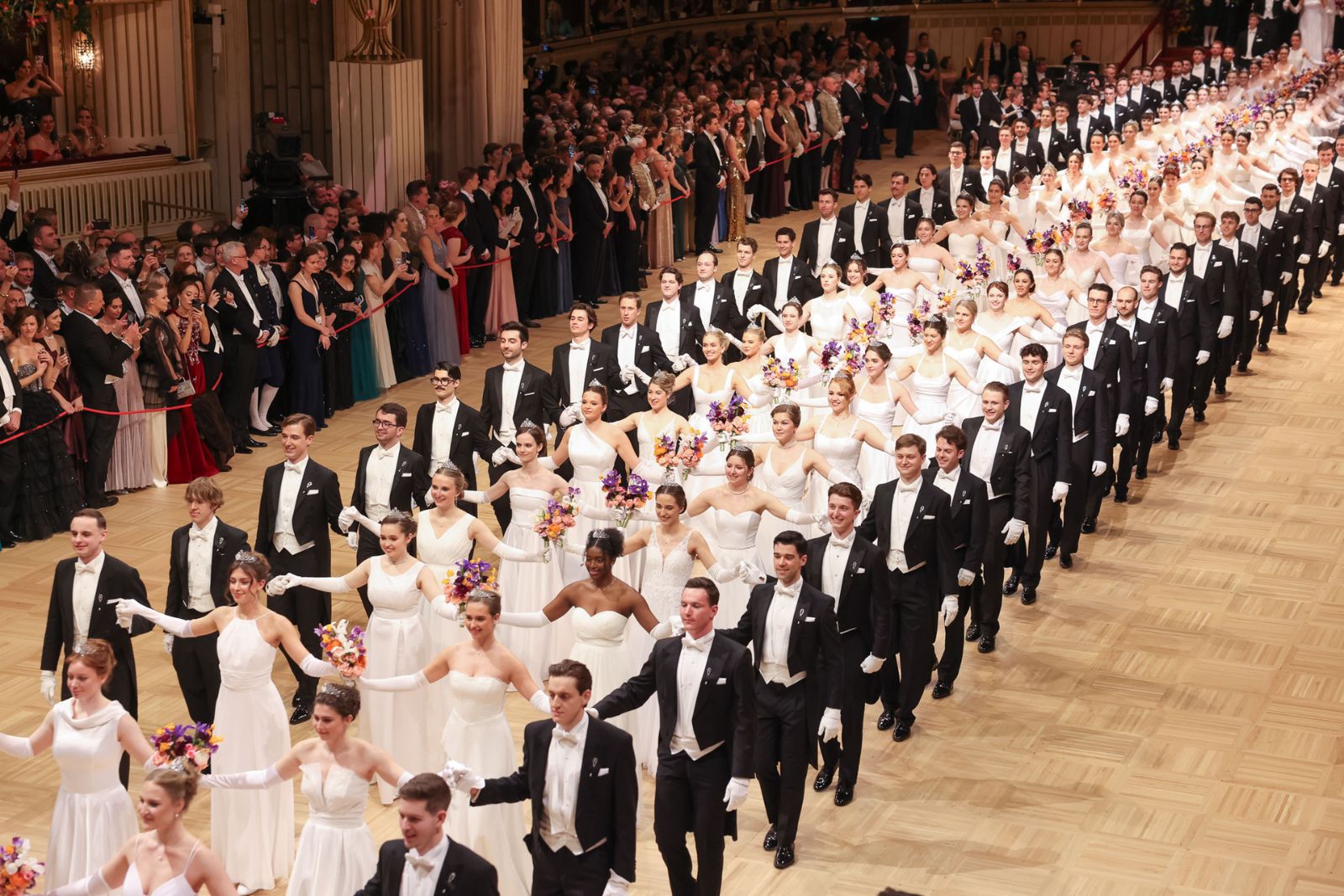 The opening committee entering in procession, debutantes in white with bouquets on the arms of partners in white tie, at The Vienna Opera Ball