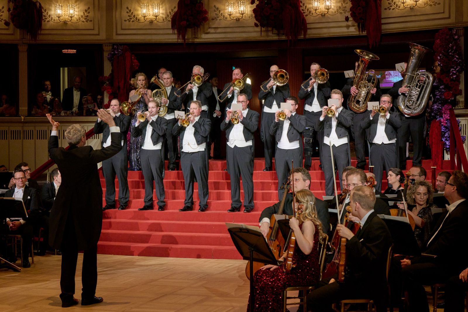 Brass players in white tie sounding the opening fanfare from the red steps above the orchestra at The Vienna Opera Ball
