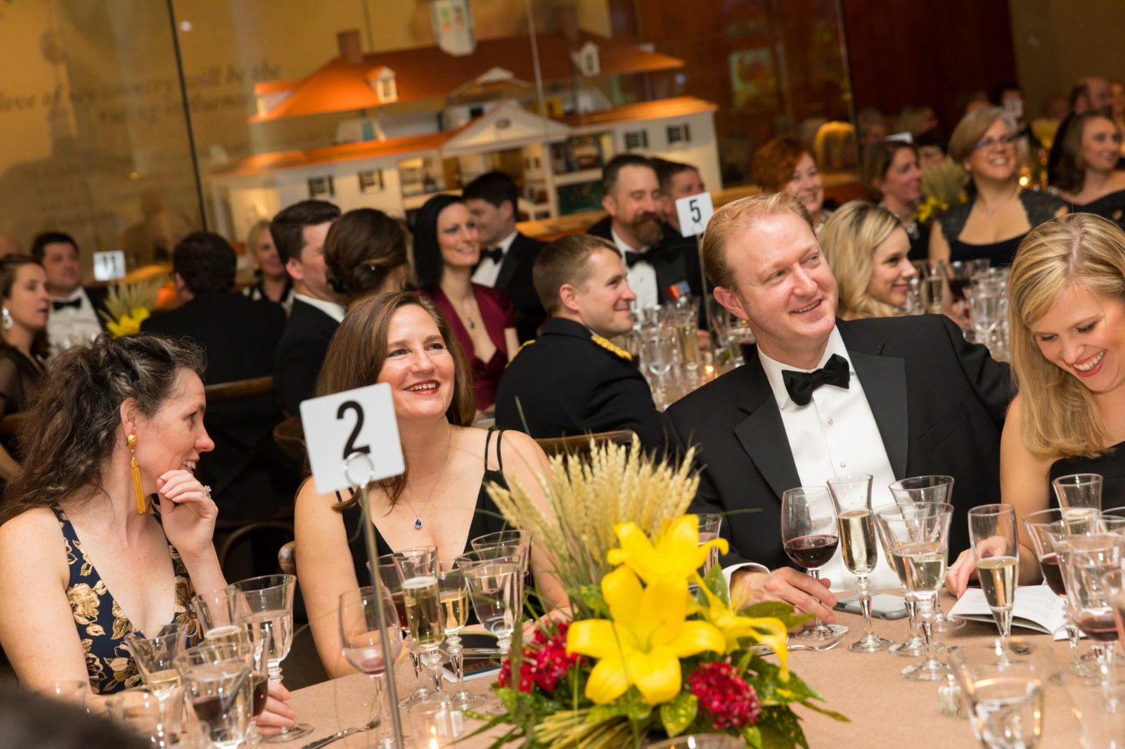 Round tables laid with candles and posies in a gilded crimson room before dinner at The Washington Birthday Ball