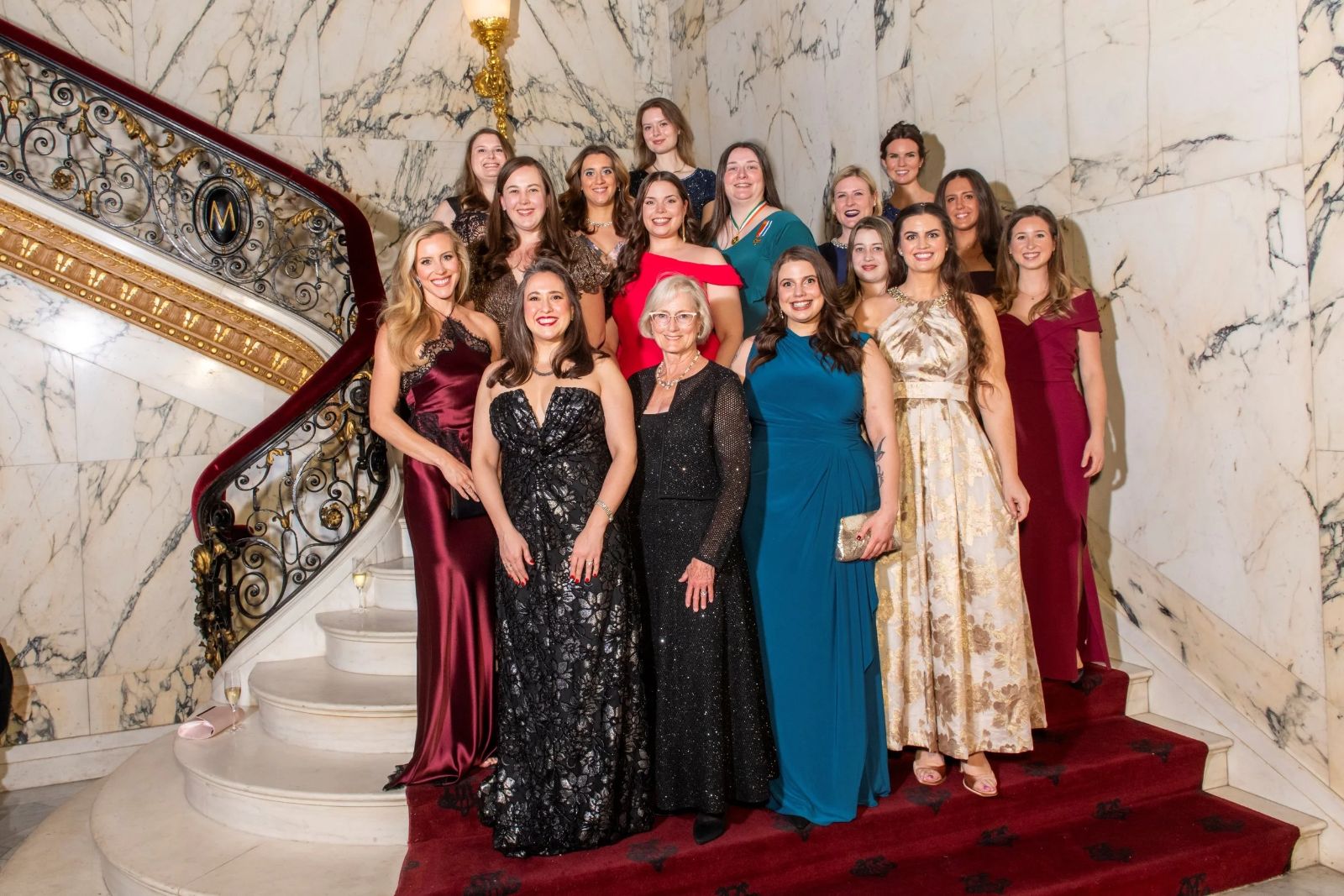 Guests in evening gowns gathered for a portrait on the marble and gilt staircase at The Washington Birthday Ball