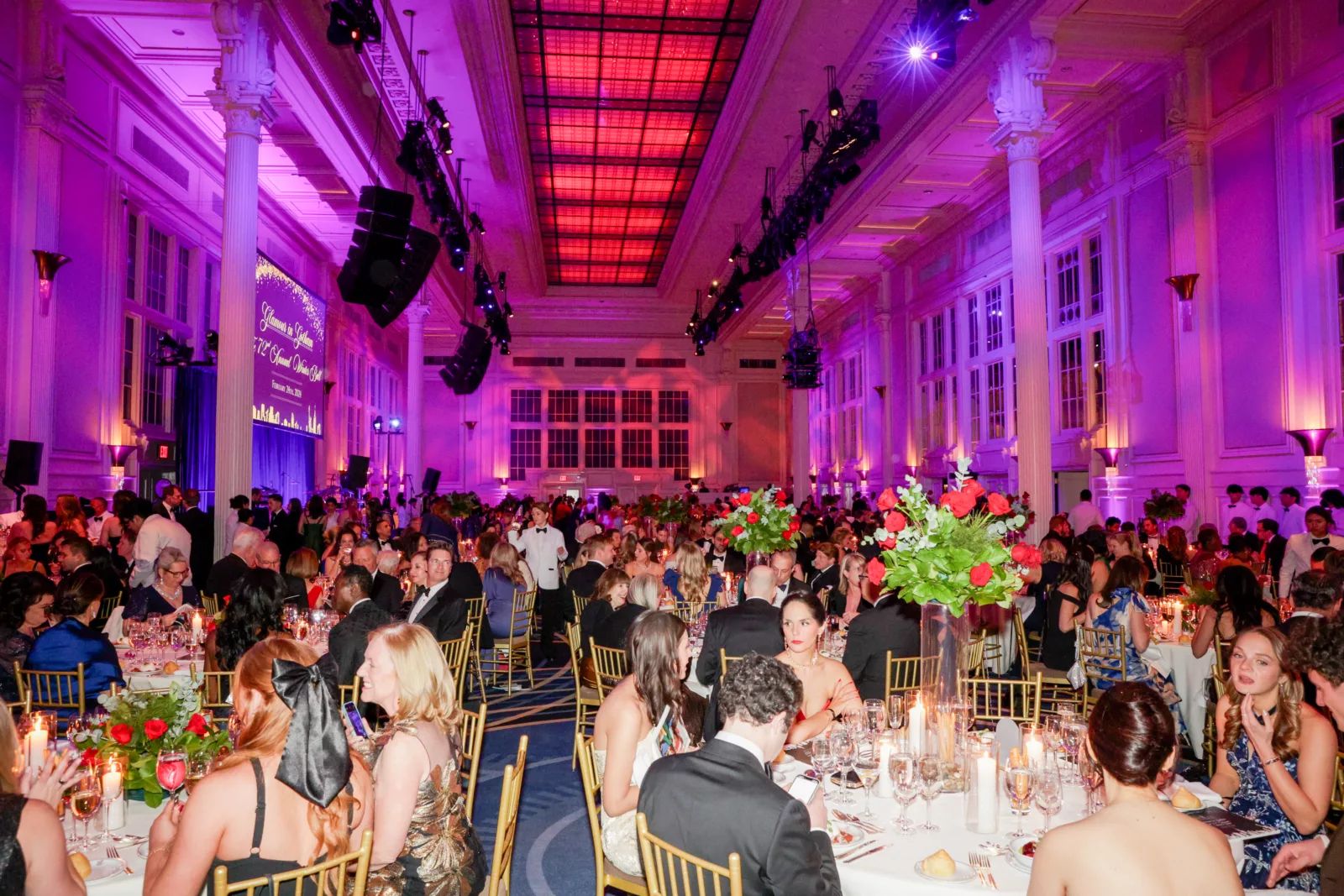 The columned ballroom lit for dinner with roses and candles at The Winter Ball, New York