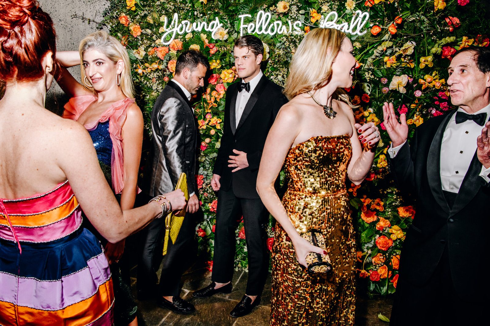 Guests in black tie before the flower wall and Young Fellows Ball sign at The Frick Collection, New York, an engagement in The Mansa Court season