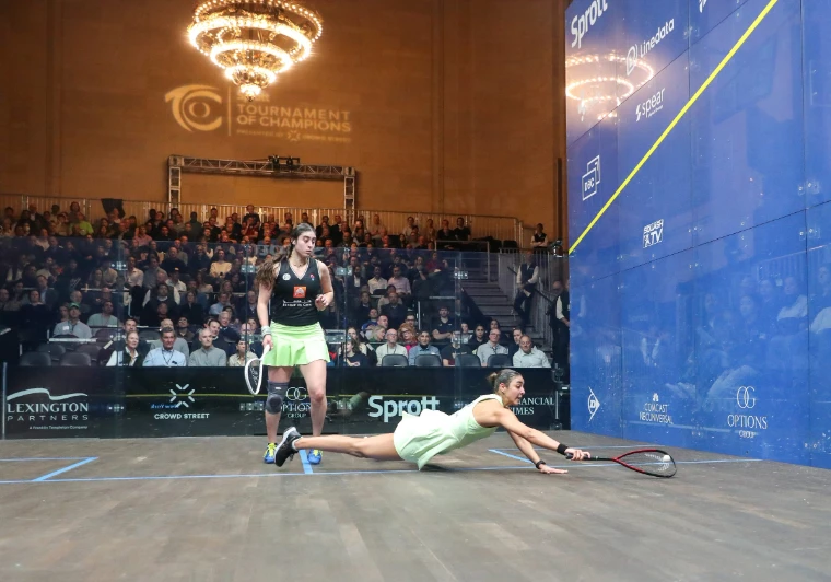 A player dives full length for the ball on the glass court. Tournament of Champions, Grand Central Terminal, New York, in the season calendar of The Mansa Court