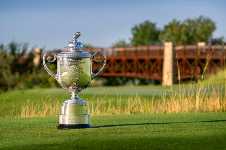 The silver Wanamaker Trophy on the tee in morning light, a timber bridge across the course behind. The PGA Championship, at US PGA Championship, in the season calendar of The Mansa Court
