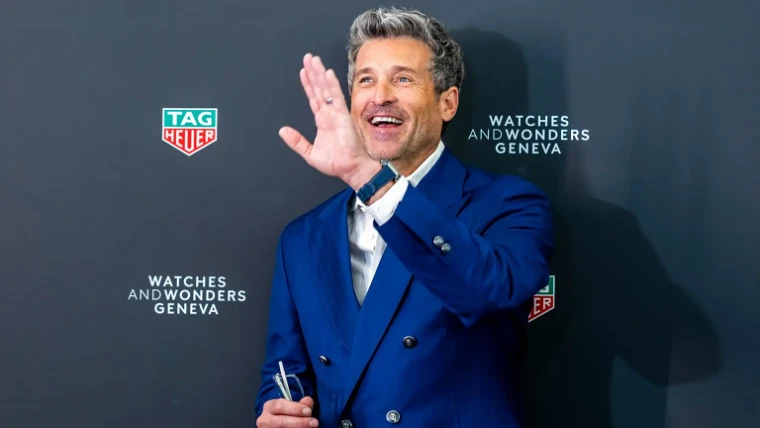 A guest in a blue double-breasted suit waving at the TAG Heuer photocall at Watches and Wonders Geneva, a mid-April engagement in the season calendar of The Mansa Court