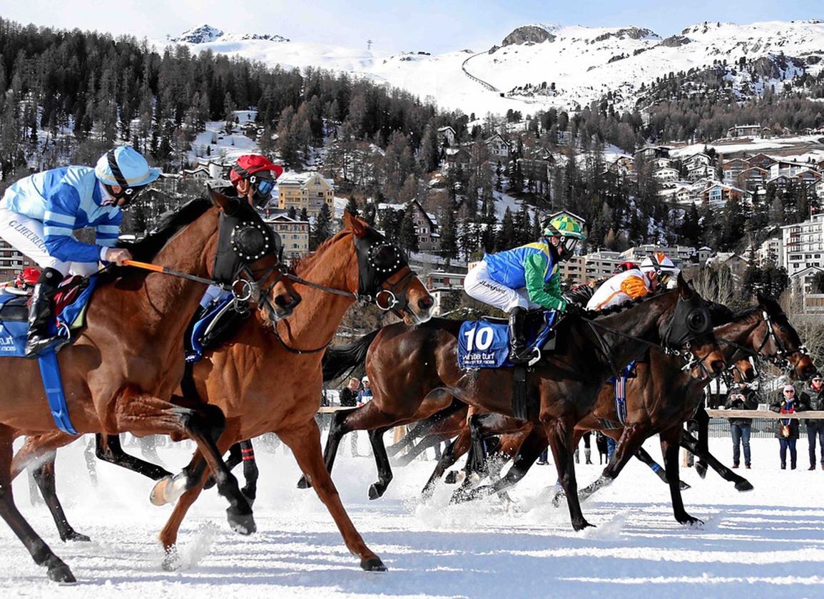 Runners passing at White Turf with the village of St. Moritz rising behind the frozen lake